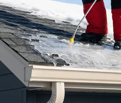 Ice dam removal technician using a steam wand to melt thick ice buildup on a residential roof in Cleveland, OH