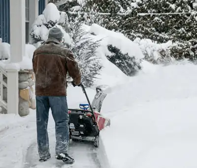 Residential snow removal technician using a snow blower to clear a home driveway and walkway in Cleveland, OH