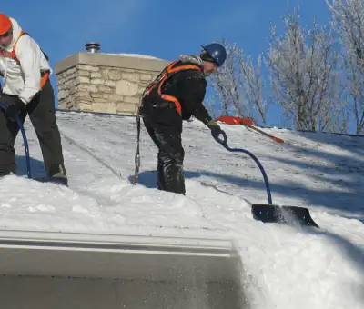 Professional technicians performing roof snow removal with safety harnesses and shovels in Cleveland, OH